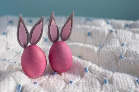 Two pink easter eggs with bunny ears close up on a white knitted blanket Stock Photos