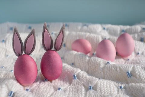 Two pink easter eggs with bunny ears close up on a white knitted blanket Stock-Fotos