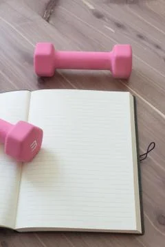 Two pink hand weights with open, blank journal, on a wood table top Stock Photos