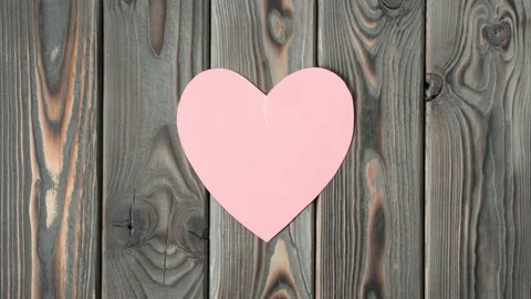 Two pink paper halves of torn heart roll and join together on wooden background 스톡 동영상 223257949
