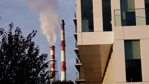 Two pipes of the heating station release white steam among modern city buildings Stock Footage 124356006