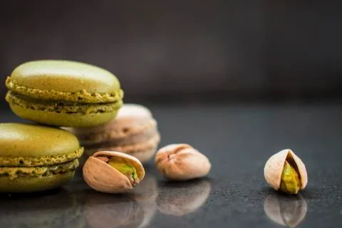 Two pistachio macarons with nuts on dark background Stock Photos