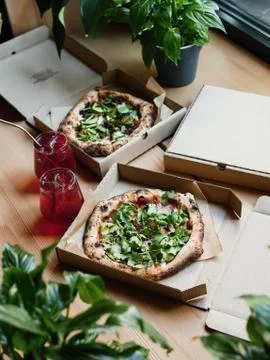 Two pizzas in boxes on a table with lemonade, flowers in the frame Stock Photos