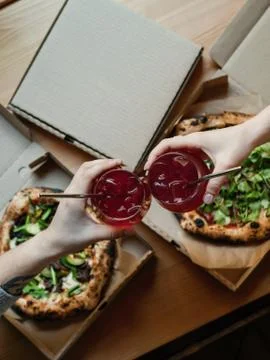Two pizzas in boxes on a table with lemonade in hands, clink glasses Stock Photos