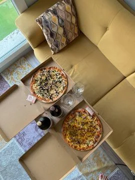 Two pizzas in open boxes with two glass bottles and glasses on a small table Stock Photos