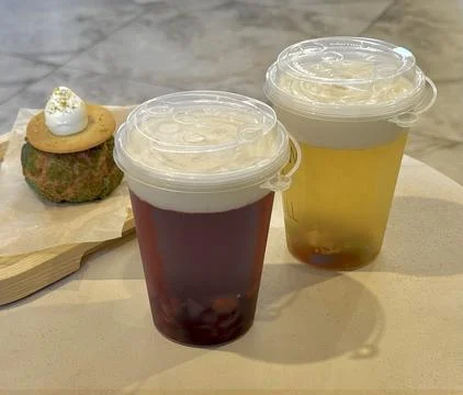 Two plastic cups with fruit bubble tea and a cake in the background, on a table Stock Photos
