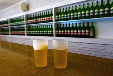 Two plastic glasses with beer on the background of bottles. Stock Photos