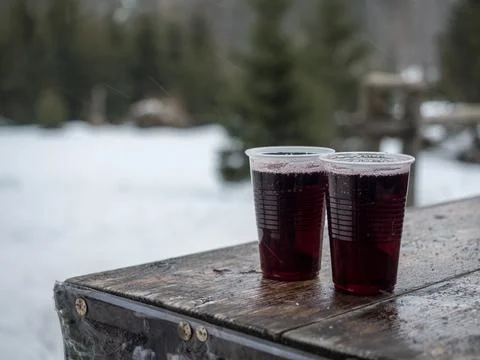 Two plastic glasses of mulled red wine on wooden table with snow on backgroun Stock Photos