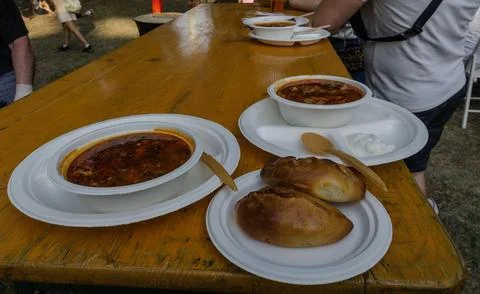 Two plastic plates with borscht and pies stand on a wooden table outside Stock Photos