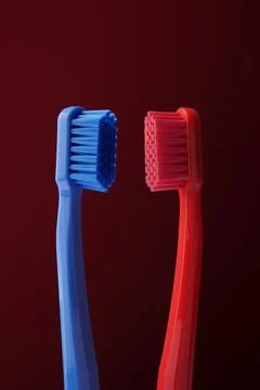 Two plastic toothbrushes red and blue on a dark red background. Oral hygiene. Stock Photos