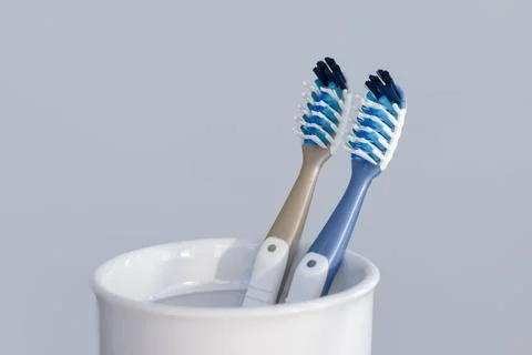 Two plastic toothbrushes in toothbrush cup closeup on grey background Stock Photos