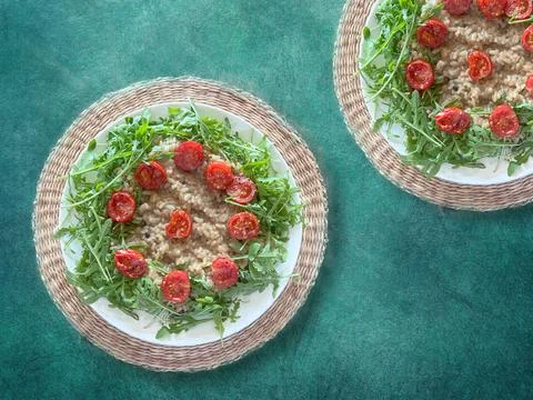 Two plates of risotto with cherry tomatoes and arugula on green background. Stock Photos