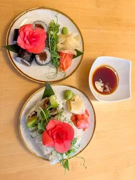 Two plates of sushi rolls with ginger wasabi and soy sauce on a wooden table  Stock Photos