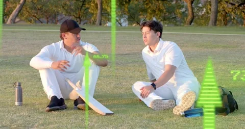 Two players sitting on grass sharing looks and talking cricket tactics on break, Stockbeeldmateriaal 327001748