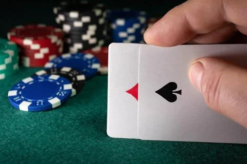 Two playing cards are held in one hand while many poker chips are stacked in  Foto stock