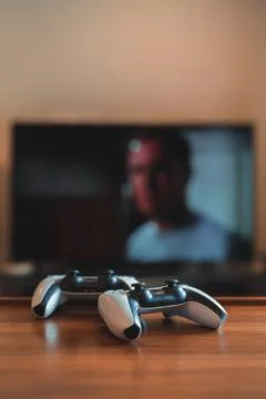 Two Playstation 5 (PS5) controllers on the table, tv on background, selective Stock-Fotos