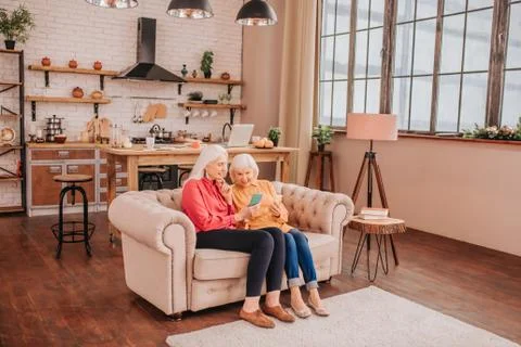 Two pleasant-looking elderly grey-haired women sitting on the sofa Stock Photos