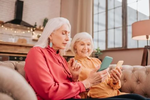 Two pleasant-looking elderly grey-haired women looking involved Stock Photos