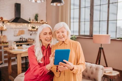 Two pleasant-looking elderly grey-haired women watching video Stock Photos
