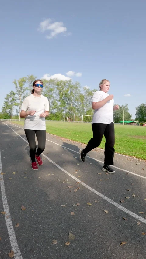 Two plus sized women jogging side by side on an outdoor track enjoy their Stock Footage 291726540