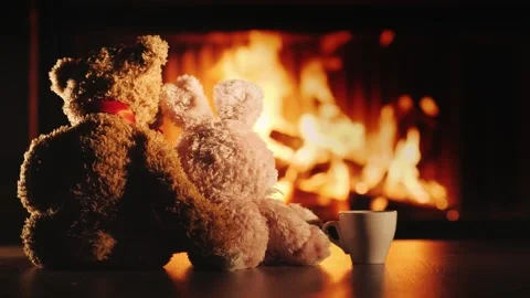 Two plush toys, a teddy bear and a bunny, embrace by a cozy fireplace with .. Video stock 334844000