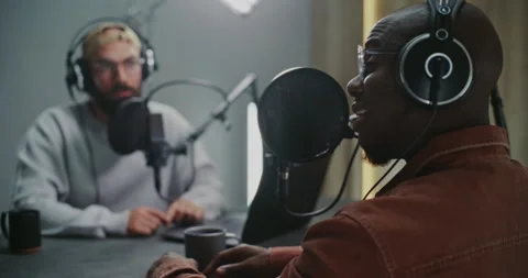 Two Podcast Hosts Sit Across Table With Laptop, Pro Microphones and Warm Drinks Video stock 322102443