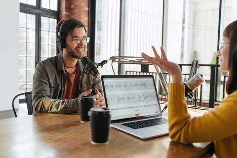 Two podcasters looking at each other while recording podcast in studio Stock Photos