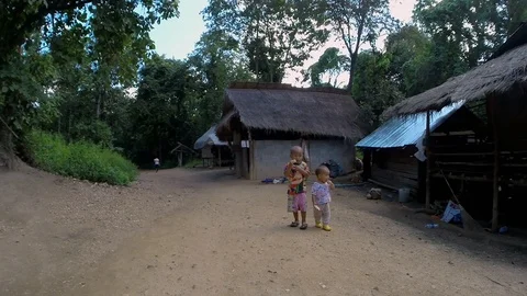 Two poor Thai children, with snacks, wondering through a run down village. Video stock 123674999