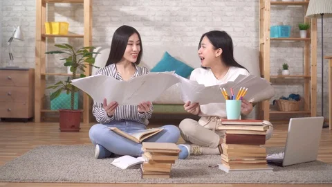 Two positive Asian students are sitting on the floor throwing papers up Stock Footage 125915161