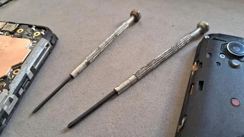 Two precision metal screwdrivers lying beside a disassembled smartphone internal Stock Photos