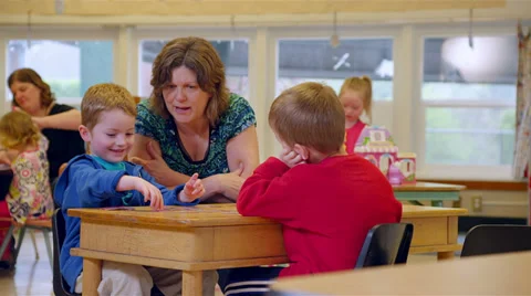 Two preschool students sit with their teacher and play the game memory with her Stock Footage 34004526