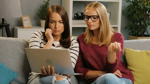 Two pretty female friends looking at something on the laptop screen and laughing Stock Footage 81924780
