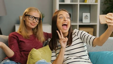 Two pretty female friends making funny selfies on the mobile phone on the couch Stock Footage 81875273