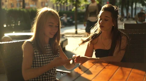Two pretty girlfriends laughing while sitting in a bar outdoors with phone Stock Footage 66261401