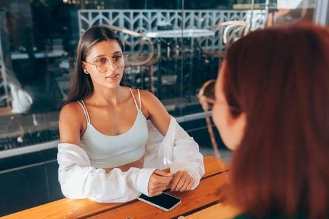 Two pretty girlfriends talking while sitting in a bar outdoors Stock Photos