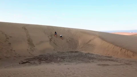 Two pretty kids are climbing on a sand dune in a desert and then tumbled down Stock Footage 95708981