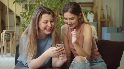 Two pretty lgbt girls are sitting on the sofa and watching some funny videos on Stock Footage 172674053