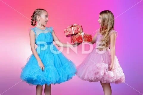 Two pretty little girls dressed in beautiful festive dresses with gift boxes Stock Photos