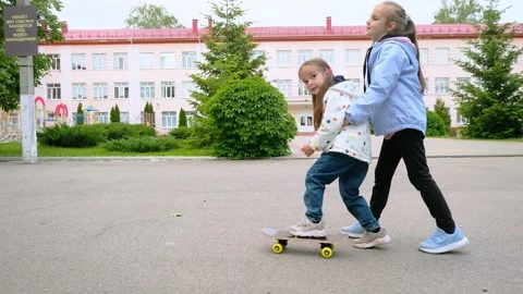 Two pretty little sisters having fun together learning to skateboard outdoors on Stock Footage 280860531