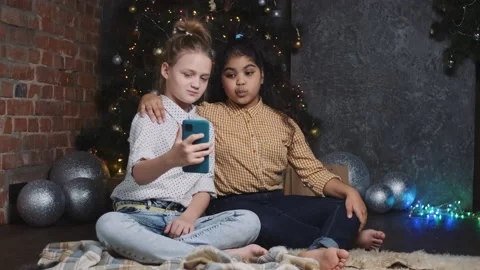 Two pretty young african and caucasian girls sitting near a New Year or 動画素材 160922814