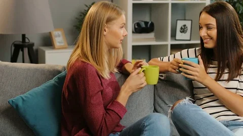 Two pretty young female friends talking and drinking tea in the cosy living room Stock Footage 81927872