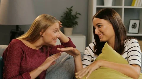 Two pretty young women talking and gossiping in the nice living room at home Stock Footage 81929787