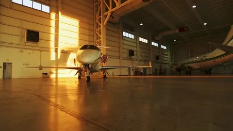 Two private jets parked inside aircraft hangar with sunset light coming in Stock Footage 78686665