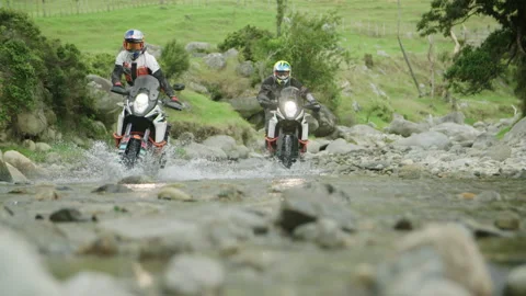 Two pro motorbiker's ride through rocky river, water splashes - Slow Motion Video stock 130296924
