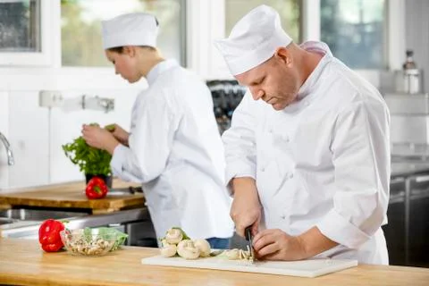 Two professional chefs preparing vegetables in large kitchen Stock Photos