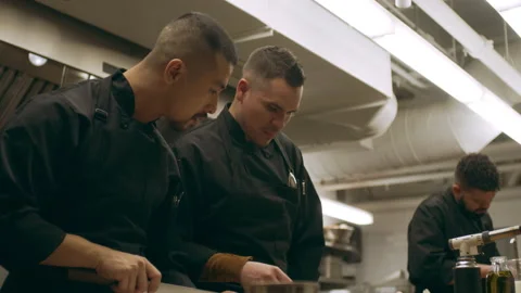 Two professional chefs talking and using a ladle to pour liquid into a bowl in i Stock Footage 199458105