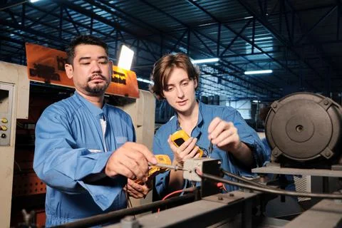 Two professional engineers inspect machines' electric systems at the factory. Stock Photos