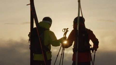 Two professional freeride skiers hugging while watching sunrise in Swiss Alps Stock Footage 129086694
