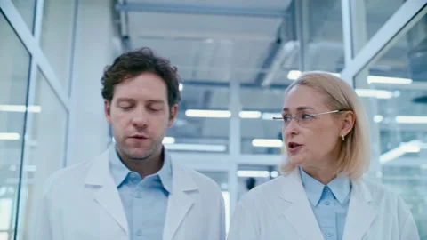 Two Professional Scientists Walking through Laboratory Hallway and Talking Stock Footage 332670950
