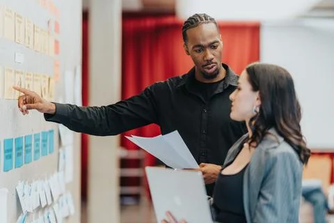 Two professionalism-oriented colleagues discussing strategy while referencing a Stock Photos